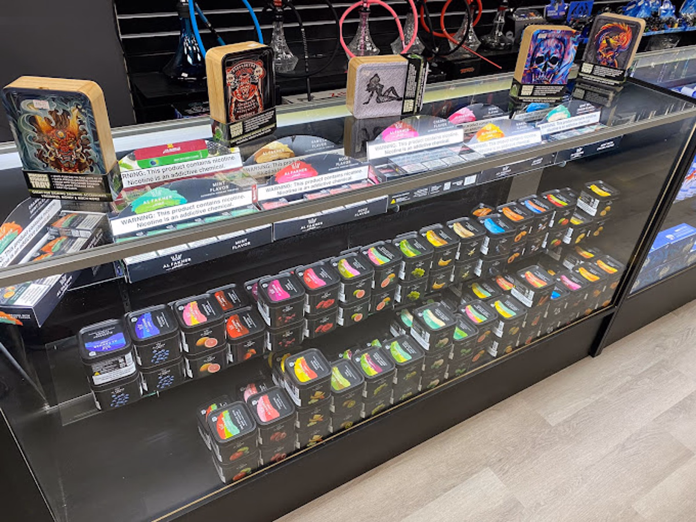 Shisha tins and hookah tobacco in the counter display case at Metro Smoke Shop, Mount Dora